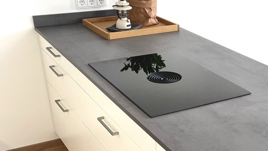 Von schräg oben fotografierte weiße Kücheninsel mit dunkelgrauer Arbeitsplatte und Griffbügeln