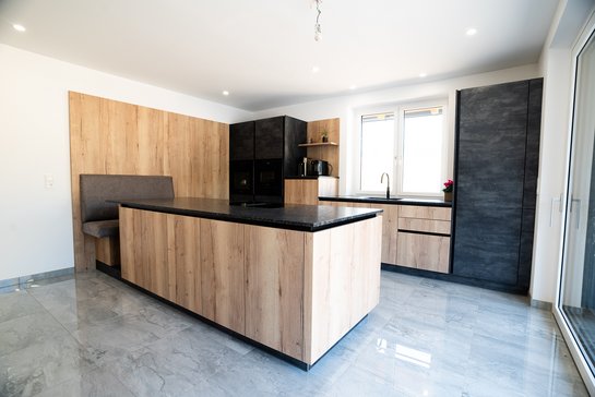 Moderne Inselküche in Holzoptik mit zwei dunkelgrauen Hochschränken und Sitzplatz an der Kücheninsel