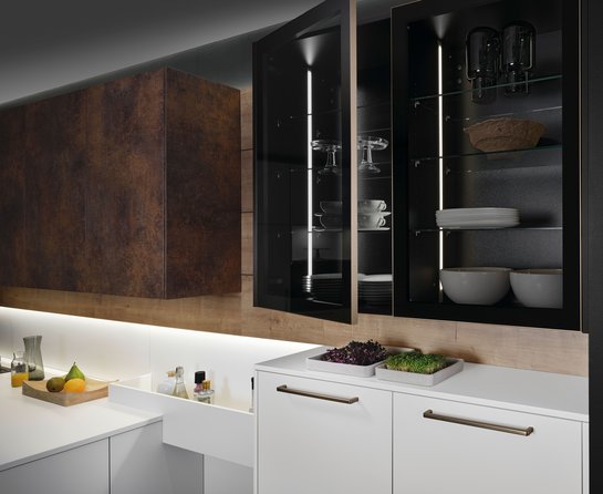 Oberschränke in patina bronze und daneben mit dunklen Vitrinentüren, darunter helle Küchenschränke