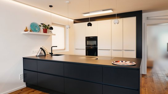 Inselküche mit Kücheninsel in dunkelgrau und Hochschrankgruppe in der Küchenzeile in weiß