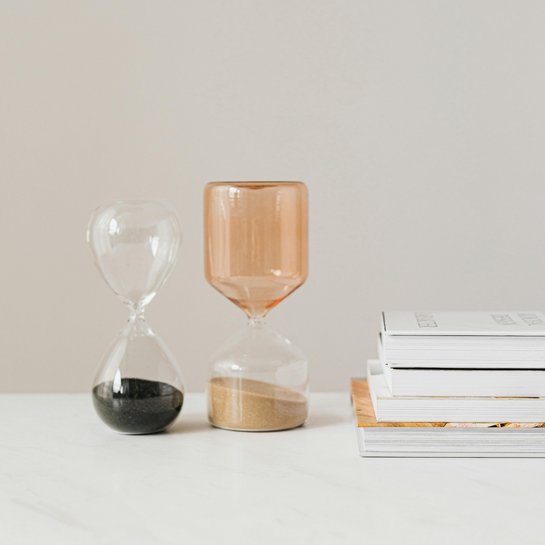 Zwei große Sanduhren stehen nebeneinander, daneben liegen Bücher.