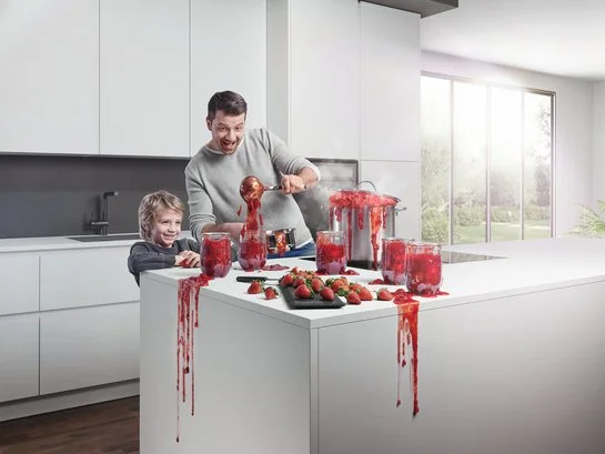 ewe nanoo® Vater und Sohn in weißer Küche beim Marmelade-Einkochen, alles tropft und spritzt