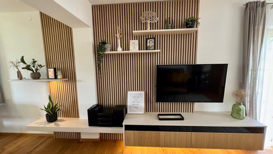 Frontansicht der TV-Wand mit offenen Boarden, Dekoration und Fernseher, kombiniert mit der vertikalen Holzlamellenoptik.