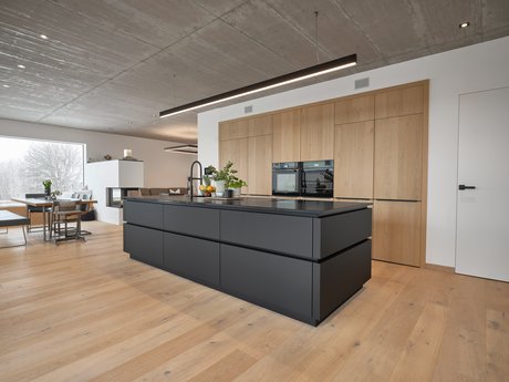 schwarze Kücheninsel mit umlaufender Griffmulde, dahinter deckenhohe Hochschränke mit Holzfronten