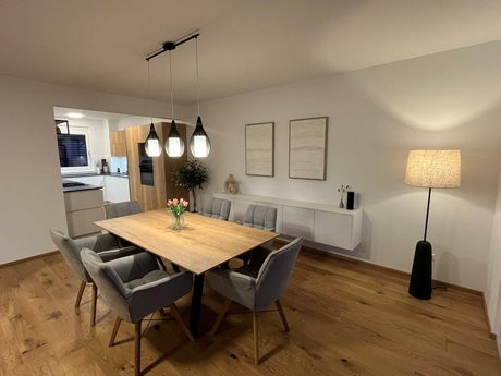 Esstisch aus Holz mit grauen Sesseln, dahinter ein weißes Sideboard