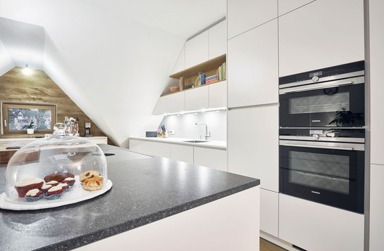 Ausschnitt einer weißen Inselküche mit dunkler Arbeitsplatte aus Stein