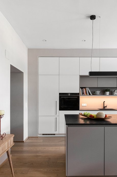 Ausschnitt einer Inselküche mit weißen Hochschränken und davor einer hellgrauen Kücheninsel