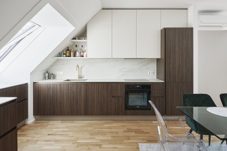 Harmonische Planung unter der Dachschräge mit Unterschränken in nuss pavia, Oberschränken in panna und goldfarbener Armatur als edlem Akzent.