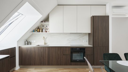 Harmonische Planung unter der Dachschräge mit Unterschränken in nuss pavia, Oberschränken in panna und goldfarbener Armatur als edlem Akzent.