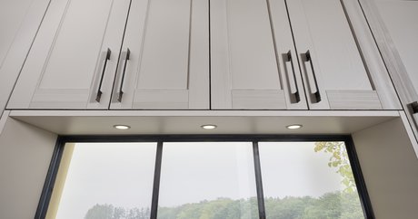 Weiße Landhaus-Oberschränke über einem Fenster mit schwarzem Rahmen