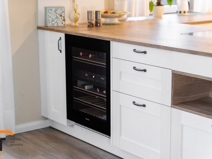 Detailbild einer Kücheninsel mit weißen Landhausfronten, einer Nische und einem Weinkühlschrank