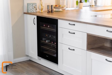 Detailbild einer Kücheninsel mit weißen Landhausfronten, einer Nische und einem Weinkühlschrank