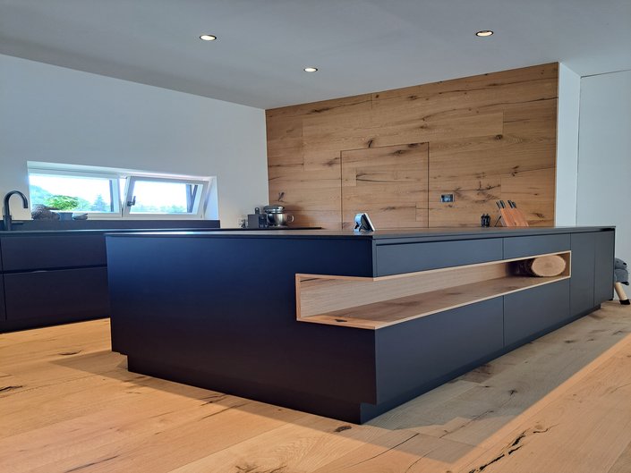 Kücheninsel in schwarz mit großer, niedriger Nische mit Holzverkleidung