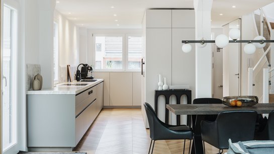 Helle Küche mit Küchenzeile links und Hochschrankgruppe rechts, davor eine dunkle Essgruppe