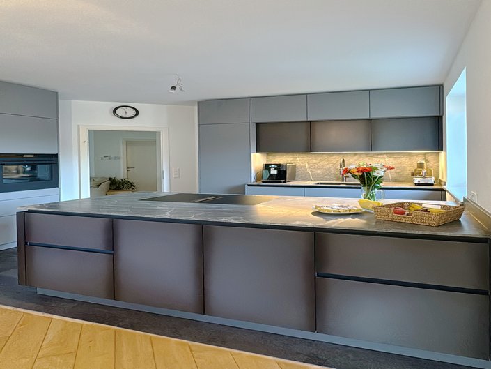 Kücheninsel in Schwarzblech-Optik, dahinter Oberschränke in grau