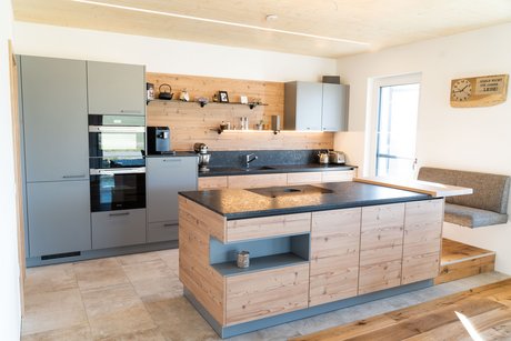 Kücheninsel in kiefer mit grauer Nische, dahinter eine Küchenzeile in grau