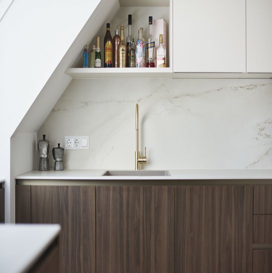 Der elegante Spülenbereich überzeugt mit flächenbündiger Spüle, goldfarbener Armatur und einer Nischenrückwand im Keramik-Look.