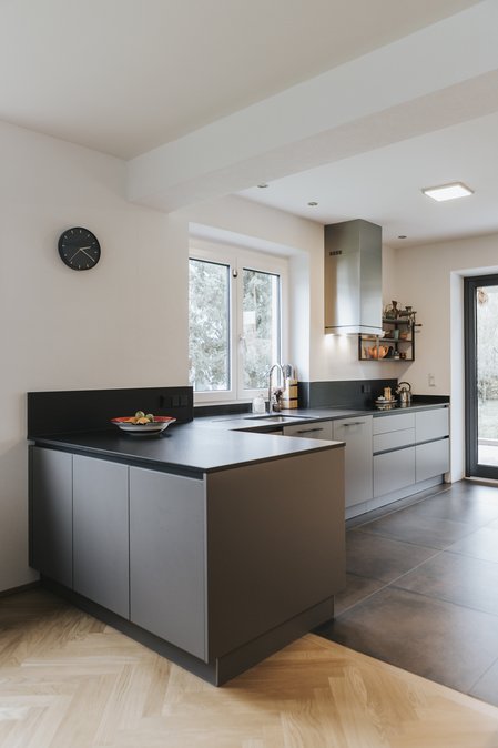 Küchenzeile in grau mit kleinem Eck, schwarze Arbeitsplatte, dahinter ein Fenster