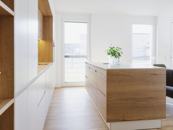 Blick in eine Inselküche mit weißen Fronten, die mit Eichenholzelementen kombiniert wurden.
