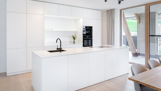 Weiße Inselküche mit heller Steinarbeitsplatte, dazu schwarze Küchengeräte