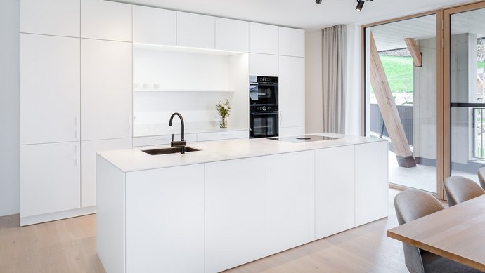 Weiße Inselküche mit heller Steinarbeitsplatte, dazu schwarze Küchengeräte