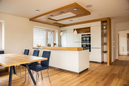 Weiße Inselküche mit dekorativen Holzelementen, davor ein Esstisch mit blau bezogenen Stühlen