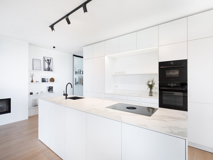 Weiße Küche mit heller Steinarbeitsplatte, dazu schwarze Küchengeräte