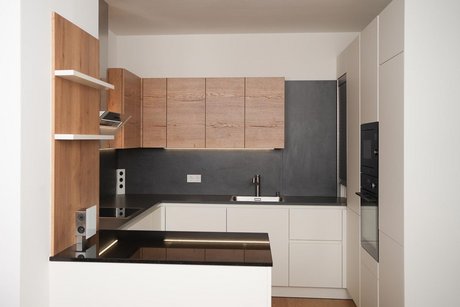 In kleinen Raum eingebaute U-förmige Küche in weiß mit dunkler Arbeitsplatte und holzfarbenen Oberschränken