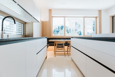 ewe nanoo® in steinweiß | Norz Interieur Sicht durch eine weiße Inselküche mit schwarzen Griffleisten und dunkler Arbeitsplatte