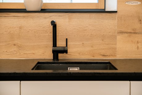 Detailfoto einer schwarzen Spüle mit schwarzer Armatur in dunkler Arbeitsplatte auf weißer Küche