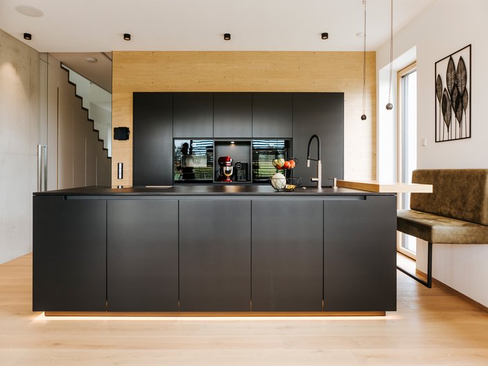 Anthrazitgraue Inselküche, die Hochschrankgruppe im Hintergrund ist mit Holz eingerahmt