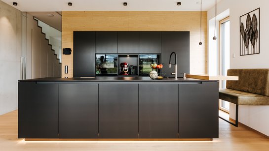 Anthrazitgraue Inselküche, die Hochschrankgruppe im Hintergrund ist mit Holz eingerahmt
