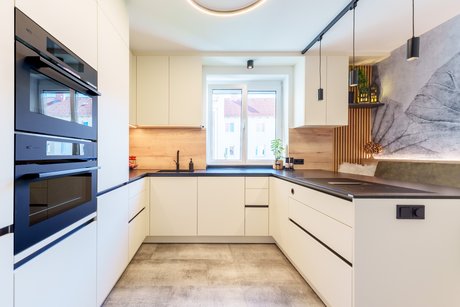 Gesamtansicht der Küche mit Hochschränken, hochgestellten Elektrogeräten und flächenbündiger Spüle.