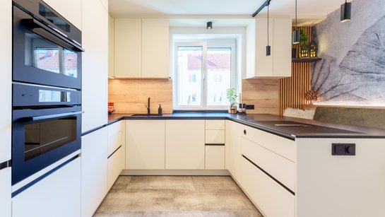 ewe nanoo® in beige | Wall Wohnen Gesamtansicht der Küche mit Hochschränken, hochgestellten Elektrogeräten und flächenbündiger Spüle.