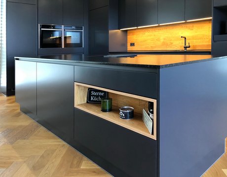 Kücheninsel und Küche in dunkelgrau/anthrazit mit holzverkleideter Nische