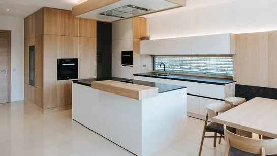 Weiße Inselküche mit Thekenplatte aus Holz und passenden Holzfronten der Hochschränke, rechts ein Esstisch