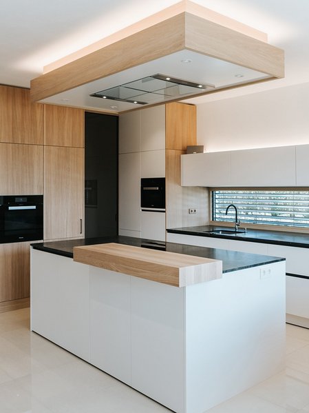 ewe nanoo® in steinweiß | Norz Interieur Weiße Inselküche mit Thekenplatte aus Holz und passenden Holzfronten der Hochschränke, rechts ein Esstisch