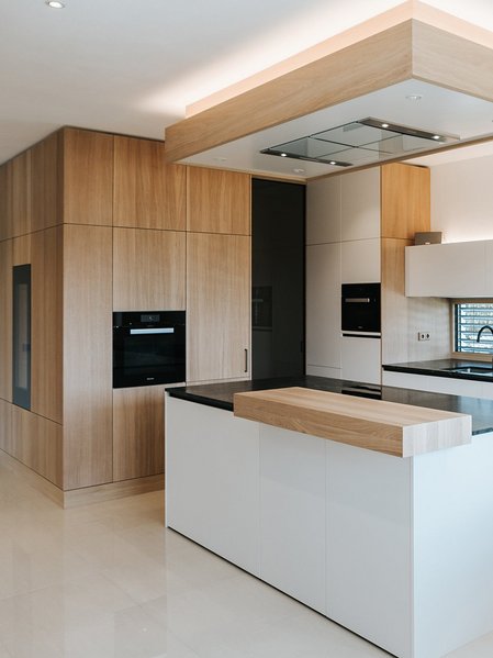 Weiße Inselküche mit Thekenplatte aus Holz und passenden Holzfronten der Hochschränke, rechts ein Esstisch