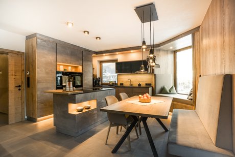 Inselküche in Betonoptik mit Holzelementen, davor eine moderne Esstischgruppe