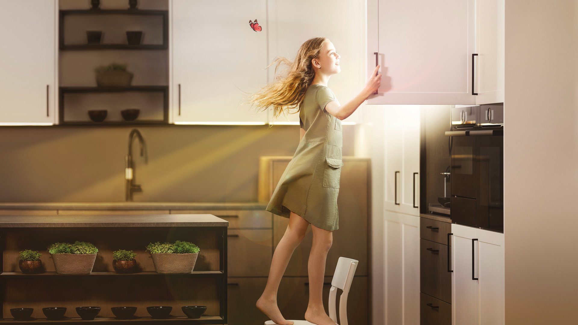 ewe - die Küche für morgen Ein Mädchen steht in einer Küche auf einem Stuhl und öffnet einen Oberschrank, daraus scheint die Sonne.