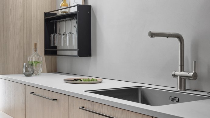 Ausschnitt einer Küchenzeile mit Spüle, hellen Holzfronten und messingfarbenen Griffen