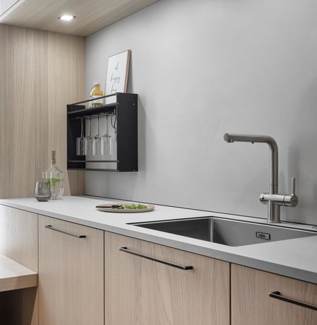 Ausschnitt einer Küchenzeile mit Spüle, hellen Holzfronten und messingfarbenen Griffen