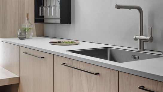 Ausschnitt einer Küchenzeile mit Spüle, hellen Holzfronten und messingfarbenen Griffen