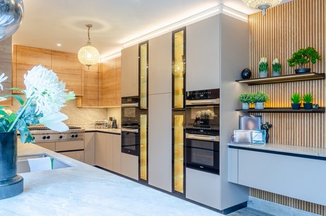 Hochschrankwand mit integrierten Geräten und beleuchteten Glasvitrinen als eleganter Blickfang.