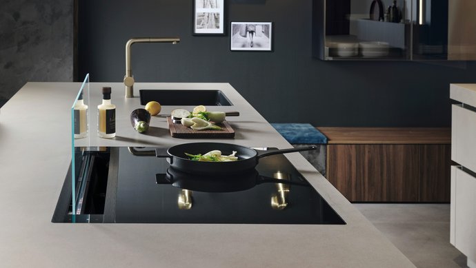 ewe Cemento . ewe Sintesa in malta grigio . nuss pavia, Kochfeld Helle Arbeitsplatte mit Kochplatte und schwarzer Spüle dahinter vor einer schwarzen Wand mit Dekoration