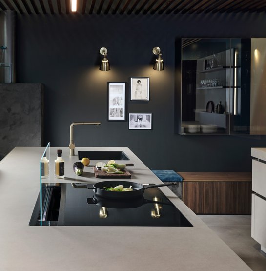 Helle Arbeitsplatte mit Kochplatte und schwarzer Spüle dahinter vor einer schwarzen Wand mit Dekoration