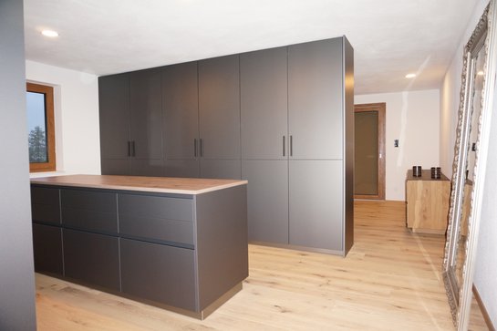 moderne Inselküche mit ewe nanoo® Küchenoberfläche in dunklen Farbtönen und Holzelementen