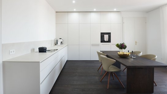 Minimalistische weiße L-förmige Küche mit dunklem Esstisch in der Mitte
